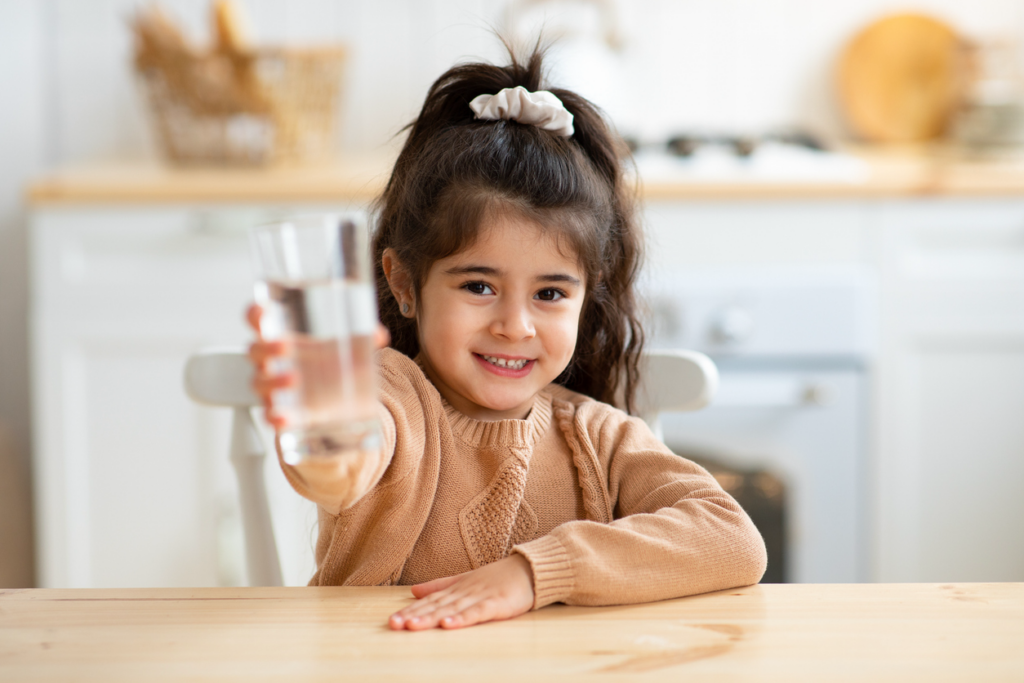 Pretty little girl smiling and holding out a glass of water.